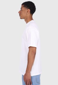 Hvid kortærmet t-shirt med rund hals, lavet af bomuld, der har en afslappet pasform og subtil sy-inddetail, båret med lyseblå jeans.