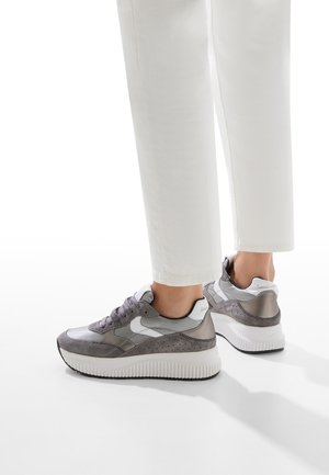 Sneaker grigi e bianchi con un mix di materiali lisci e testurizzati, punta arrotondata, suola bianca spessa e accenti perforati.