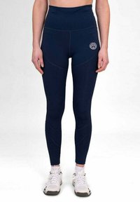 Leggings alta vita di colore blu navy realizzati in materiale elastico, con dettagli delle cuciture e un logo sull'anca, abbinati a scarpe sportive bianche.