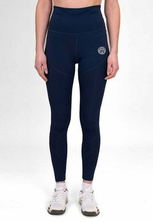 Leggings de tiro alto en azul marino, confeccionados en material elástico, con detalles de costura y un logo en la cadera, combinados con zapatillas deportivas blancas.