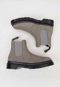 Harmaat mokkasiinit nilkkavöillä, mustilla kumipohjilla ja keltaisilla vetonauhoilla, joissa on sileä pinta ja pyöreä kärkiprofiili.