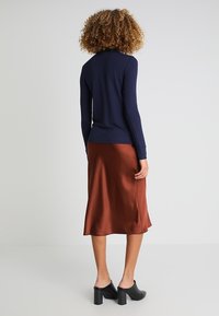 Maglietta a maniche lunghe blu navy abbinata a una gonna midi in satin color ruggine. L'outfit presenta texture morbide e una silhouette aderente. Scarpe con tacco a blocco nere.