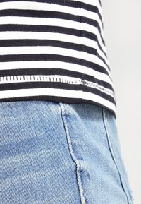 Koszulka w czarno-białe paski z obszytym dołem, zestawiona z jasnoniebieskimi dżinsami, na których widać szczegóły szycia.