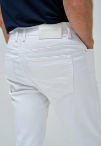 Vaqueros de mezclilla blanca con una textura suave, con bolsillos traseros y una etiqueta de cuero que dice "SALSA JEANS" en la cinturilla.