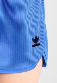Blue ribbed athletic shorts with a curved hem, featuring a black Adidas logo on the left side. Smooth texture and elastic material.