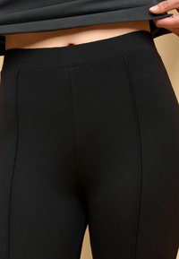 Černé legíny s vysokým pasem vyrobené z elastického materiálu, s hladkou texturou a jemnými švy na přední straně.