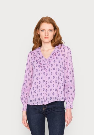 Blusa lilás clara com decote franzido, apresentando uma estampa de flores e geométrica em roxo escuro, e mangas franzidas. Estilizada com jeans escuros.