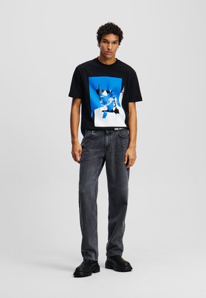 T-shirt graphique noir avec un imprimé bleu et blanc au design abstrait. Associé à un jean droit gris et des bottes noires à semelles épaisses.