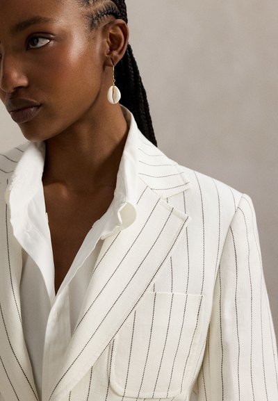 Λευκό σακάκι με λεπτές ρίγες και γιακά με εγκοπή, εμπρός τσέπη, και λευκό πουκάμισο με γιακά· συνοδευόμενο από χρυσό σκουλαρίκι με λευκό κοχύλι.