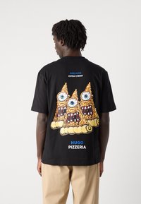 Svart t-skjorte med et fargerikt grafisk design av tre pizzastykker med øyne og munner. Teksten sier "PIZZA KJÆRLIGHET" og "HUGO PIZZERIA."