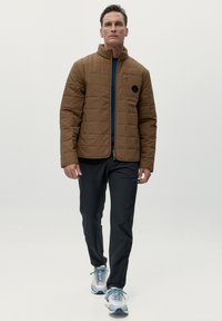 Giubbotto trapuntato marrone con colletto alto, strato interno blu e pantaloni neri. Scarpe da ginnastica bianche e blu completano l'outfit.