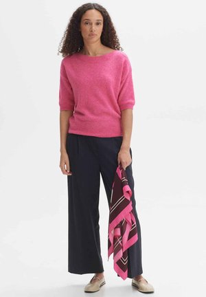 Pink short-sleeve sweater with a wide neckline, paired with navy wide-leg pants. Holding a brown and pink patterned scarf.