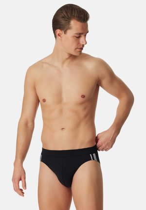 Slip da uomo in cotone nero con texture liscia, dotati di una fascia larga in vita e due strisce argento sui lati. I design sono minimalisti e funzionali.