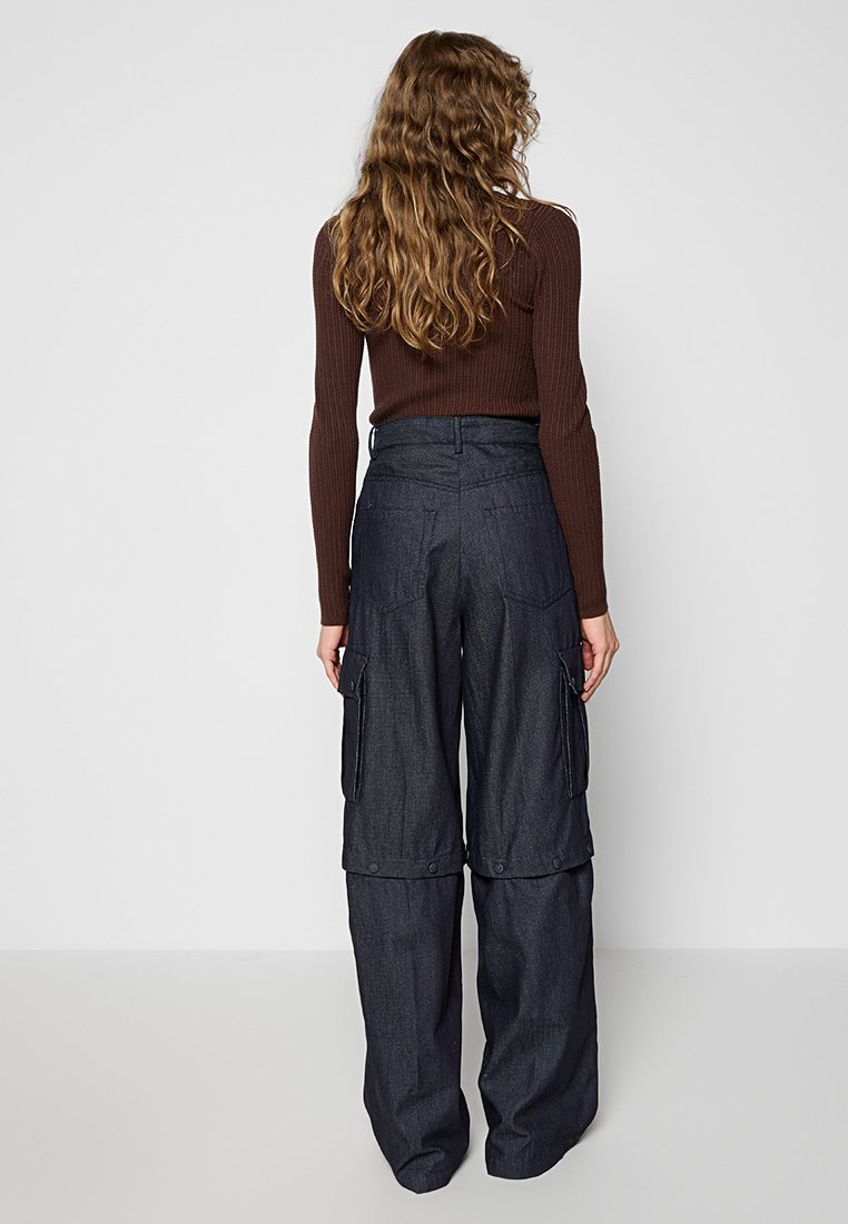 Cargo-jeans in donker denim met brede pijpen, meerdere zijzakken en een hoge taille. Een geribbelde bruine lange mouw top is ook zichtbaar.