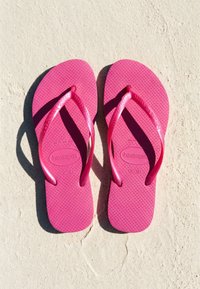 Ζευγάρι φωτεινά ροζ σαγιονάρες Havaianas τοποθετημένες δίπλα δίπλα σε μια επιφάνεια με υφή ανοιχτού χρώματος.