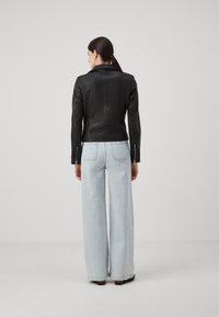 Svart skinnjakke med en tettsittende design, med slagkrage og glidelås ved ermer, kombinert med lyseblå vide jeans.