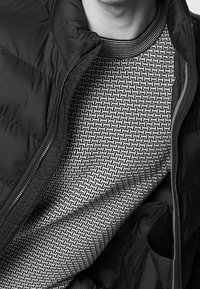 Puffer jacket in black fabric, unzipped to reveal a patterned gray sweater underneath, featuring a geometric design and contrasting ribbed collar.