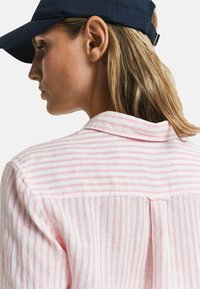 Camicia in lino con righe verticali rosa e bianche, colletto button-down, dettagli di cucitura visibili e una vestibilità rilassata visibile sulle spalle e sulla schiena.