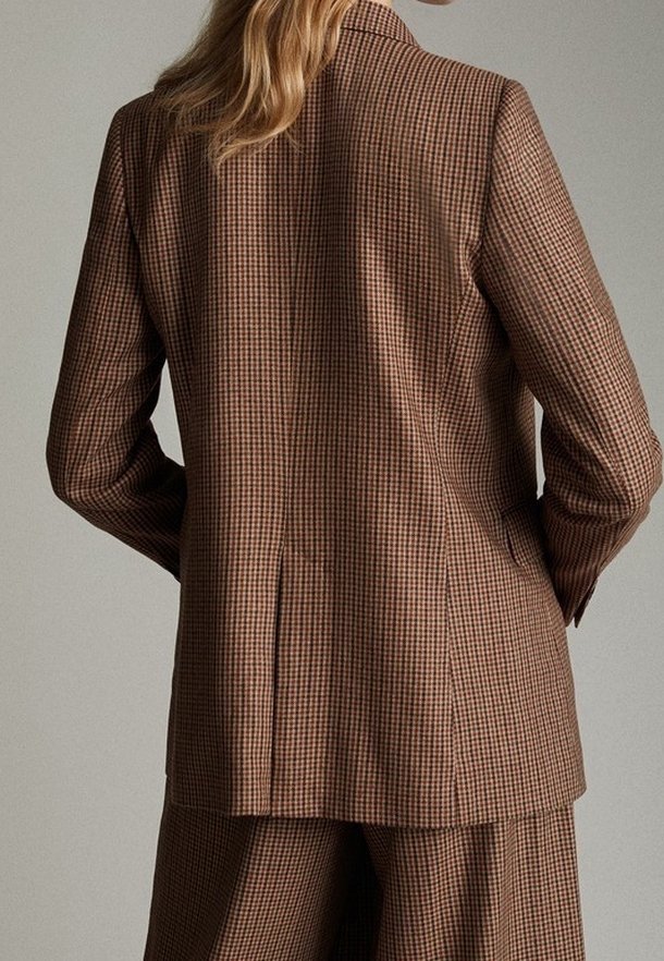 Brązowa marynarka w kratę o dopasowanym kroju, z klapami w kształcie litery "notch" oraz pojedynczym wentylem, wykonana z teksturowanej tkaniny. Widok z tyłu pokazuje detale szwów.