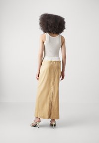 Top sans manches côtelé blanc avec taille élastique, associé à une longue jupe beige clair avec une fente arrière. Le mannequin se tient de dos par rapport à la caméra.