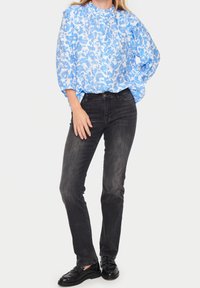 Blå och vit blommig blus med hög halsringning och puffärmar, i kombination med svarta slim-fit jeans och svarta loafers.