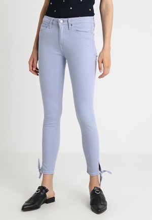 Hellblaue Skinny-Jeans mit Knöchelriemen, kombiniert mit schwarzen Slip-on-Fransen-Loafers und einem schwarzen Oberteil mit kleinen Sternmustern.
