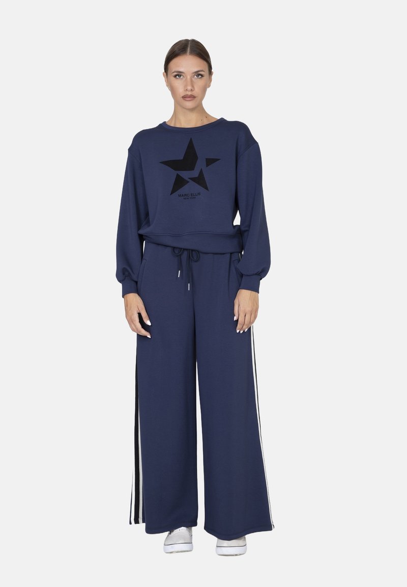 Ensemble de survêtement bleu marine avec un graphisme étoile noire, comprenant un haut ample et un pantalon à jambes larges avec des bandes latérales blanches. Tissu en mélange de coton.