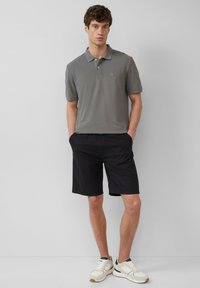 Grijze polo met een zachte textuur, gedragen met zwarte shorts en witte sneakers. Subtiel logo op de borst, comfortabele pasvorm.