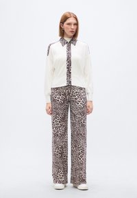 Παντελόνια με λεοπάρ σχέδιο και μπλούζα κρεμ χρώματος με γιακά και πλαϊνή ταινία με λεοπάρ σχέδιο. Το σύνολο έχει χαλαρή εφαρμογή και ελαφρύ ύφασμα.