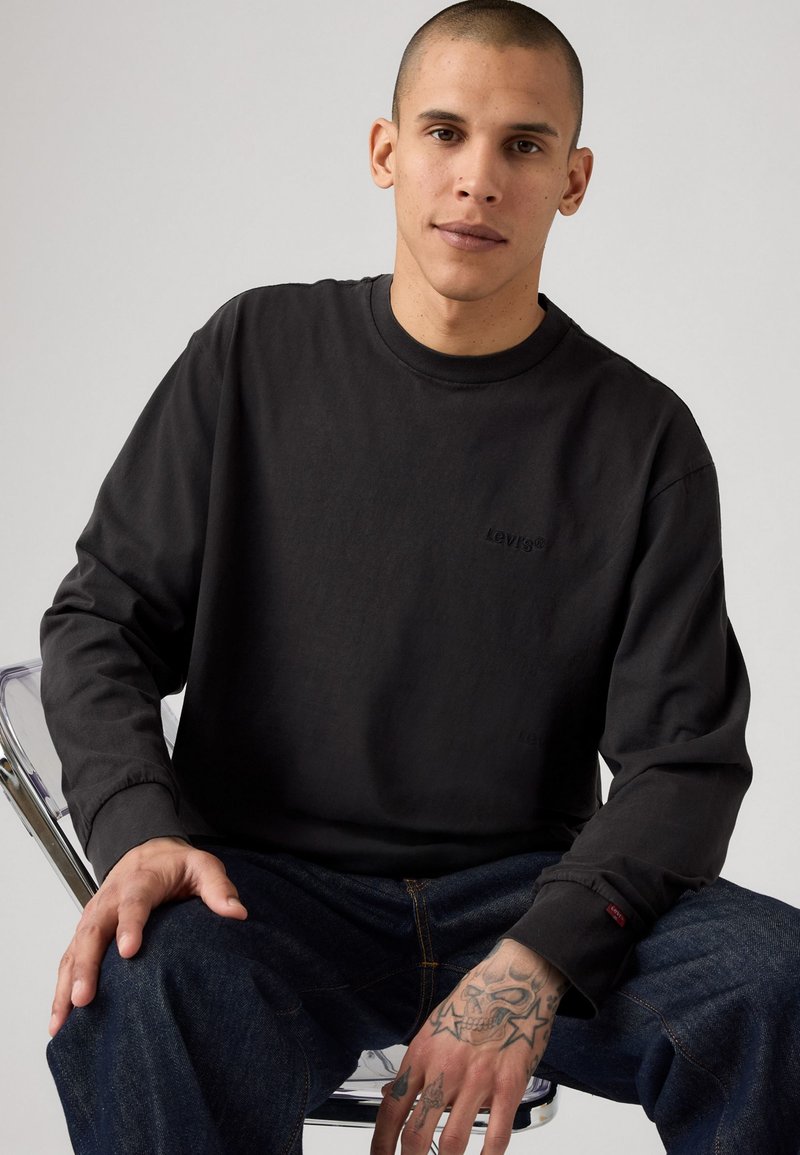 Felpa nera a maniche lunghe con logo Levi's discreto, collo tondo e polsini a costine, abbinata a jeans in denim blu scuro.