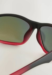 Slnečné okuliare s čiernymi a gradientnými červenými rámami, s šedými sklami. Elegantný dizajn s zakriveným tvarom a hladkým povrchom.