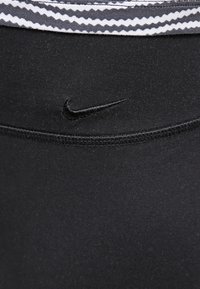Černé legíny Nike s texturovaným pasem, který má šedý a bílý zigzagový vzor, zvýrazněný malým černým logem.
