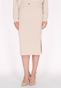 Beige gestrickter Bleistiftrock mit einem seitlichen Schlitz, kombiniert mit nudefarbenen High Heels. Der Stoff hat eine strukturierte Oberfläche und gerippte Details am Bund.