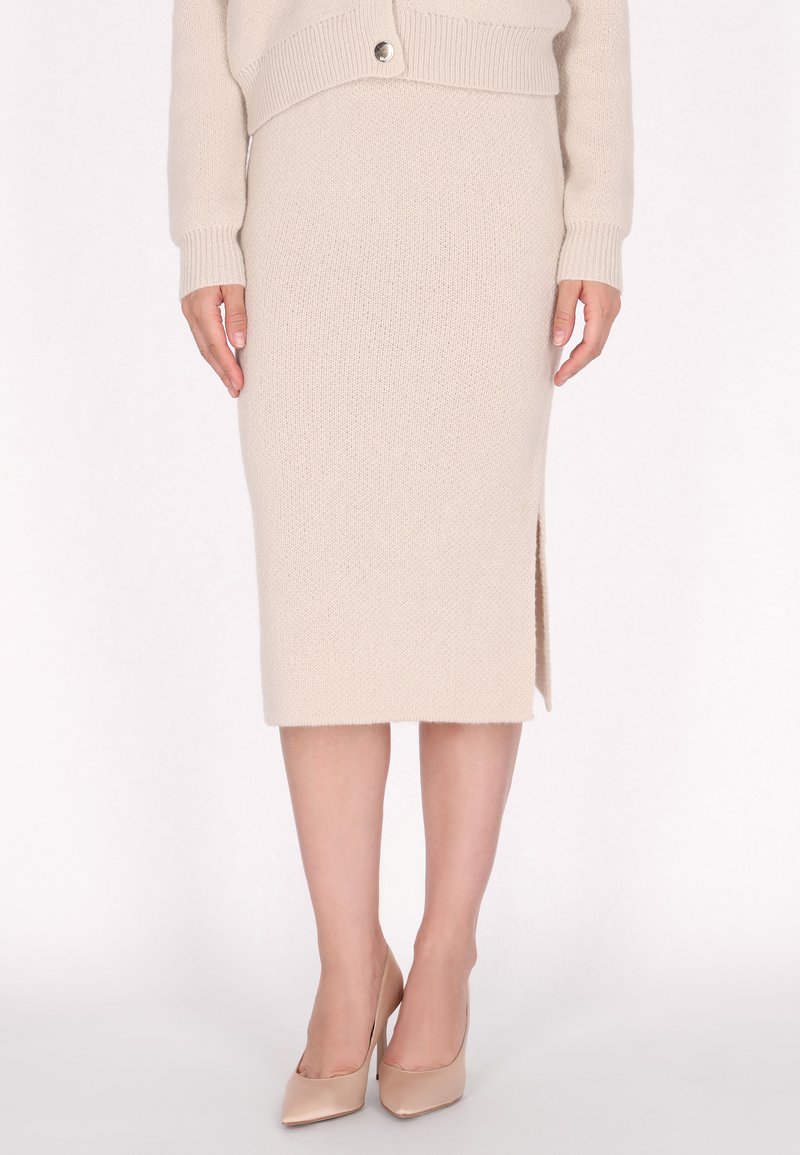 Beige gestrickter Bleistiftrock mit einem seitlichen Schlitz, kombiniert mit nudefarbenen High Heels. Der Stoff hat eine strukturierte Oberfläche und gerippte Details am Bund.