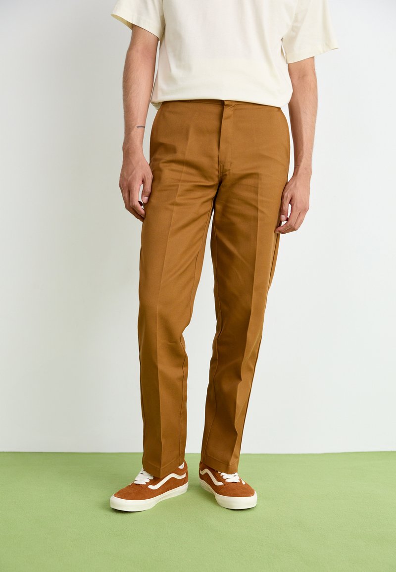 Brown trousers with a slim fit, crease details, and a smooth texture, paired with orange-brown sneakers featuring white accents.