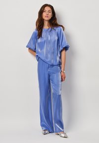 Lichtblauw, glanzend twee-delig outfit met een kortmouwtop en wijde broek. Zilveren instap schoenen maken de look compleet.