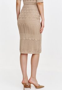 Beżowa spódnica ołówkowa dziergana, z misternymi wzorami ażurowymi i fakturowanymi, z dopasowanym stanem i długością do połowy łydki.