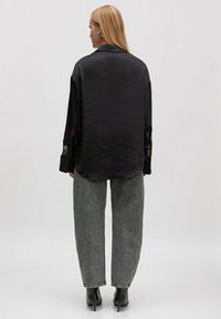 Schwarze Satinbluse mit lockerer Passform, langen Ärmeln mit Spitzenakzenten, kombiniert mit hoch taillierten, weit geschnittenen grauen Jeans und schwarzen High Heels.