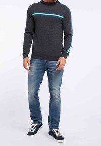 Maglione grigio a maglia con strisce blu e verdi, slim fit con scollo e polsini a costine. Abbinato a jeans azzurri e sneakers scure.