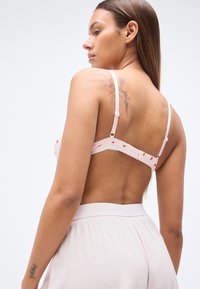 Soutien-gorge rose à pois blancs, bordé de dentelle, bretelles ajustables et fermeture à agrafes dans le dos. Tissu doux avec une légère brillance.