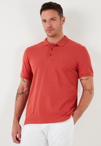 Červená polo triko s klasickým límečkem, tříknoflíkovou légou a krátkými rukávy. Hladká textura, přiléhavý střih a sportovní vzhled.