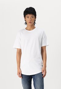 T-shirt en coton blanc à manches courtes, col rond et ourlet légèrement allongé. Associé à un jean en denim bleu.
