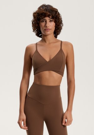 Brown activewear set featuring a wrap-style bra top with thin straps and high-waisted leggings, both in a smooth, stretchy fabric.