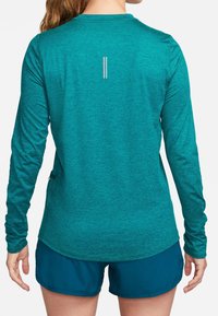 Teal long-sleeve athletic shirt with a heathered texture, rounded hem, and reflective vertical stripes on the back. Paired with dark blue shorts.