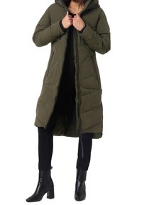 Olivgrön lång vadderad kappa med huva, frontdragkedja och sidofickor. Har svarta detaljer och en avslappnad passform. Bärs över svarta byxor och stövlar.
