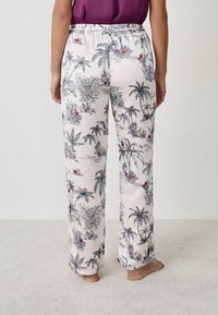 Pantaloni da pigiama leggeri e larghi di colore bianco sporco con stampa di palme e fiori neri, con vita elasticizzata e gambe dritte.