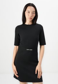 Rochie neagră cu mâneci scurte, confecționată dintr-un material neted, având o siluetă ajustată și un brâu cu logo-ul "JOOP! JEANS" în alb.