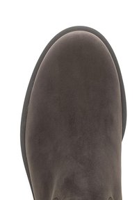 Bout de chaussure en daim marron foncé à forme arrondie et bord de semelle noire, présenté de dessus sur fond blanc.