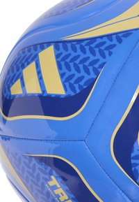 Plavi i zlatni nogometni lopta s geometrijskim i listastim uzorcima, prikazuje šivane panele i djelomični tekst marke "TR" na površini.