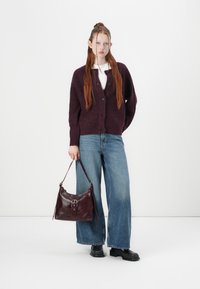 Burgundy knit cardigan with buttons, white shirt, wide-leg blue jeans, holding a dark red leather bag, and wearing black platform boots.